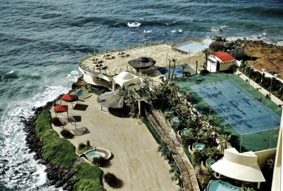 Aerial view of the Holistic Sanctuary cliffside grounds, pool and tennis court beside the Pacific