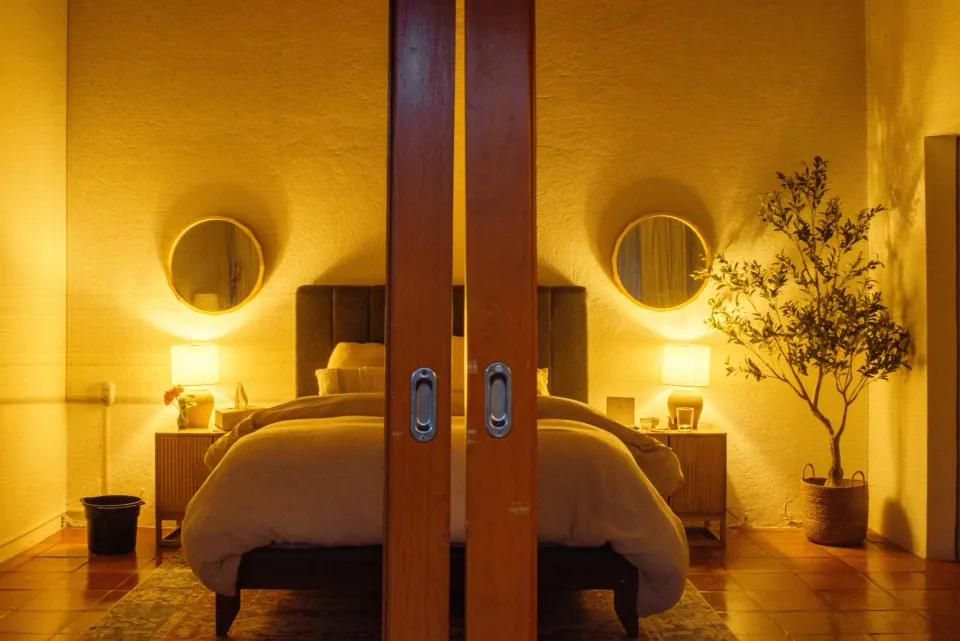 Warmly lit guest bedroom viewed through glass doors at Inner Realms Center
