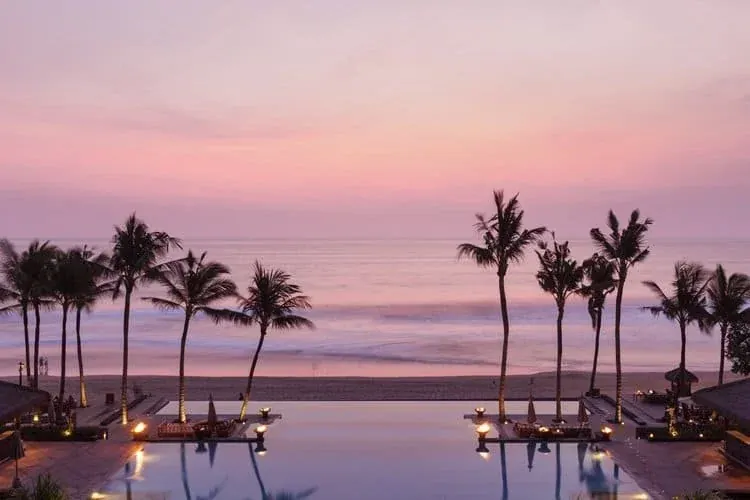 The Legian Seminyak infinity pool facing the beach and palm trees at sunset.