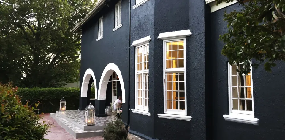 Dark-painted Sandhurst Manor building with white arched entrances and garden planting.