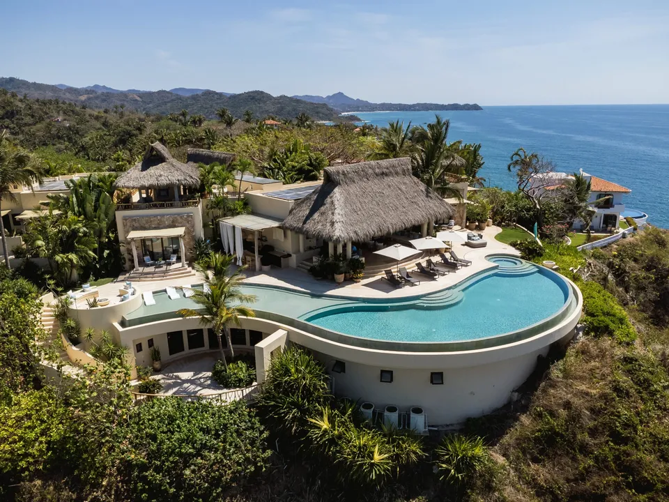 Aerial view of the Sayulita Wellness Retreat residence and curved pool beside the sea